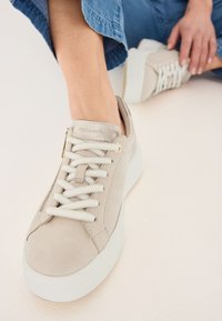 Sneaker in suede beige con suola in gomma bianca, design con lacci e dettagli dorati. Parte superiore testurizzata con finitura liscia, caratterizzata da cuciture.