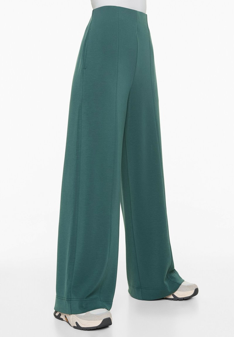 Pantalons larges verts en tissu doux avec une texture lisse, dotés de poches latérales et d'une taille haute. Accentué par une chaussure de couleur contrastante.