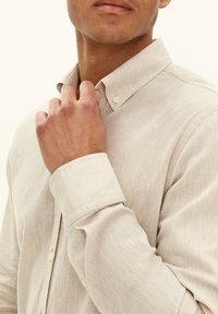 Lichtbeige linnen shirt met een kraag, gedetailleerde knopen en een relaxte pasvorm. Zichtbare textuur zorgt voor een zachte uitstraling.