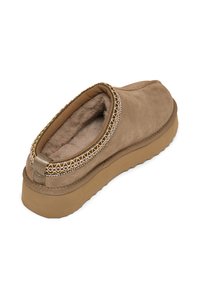 Scarpa slip-on in suede marrone con un interno morbido, cuciture decorative attorno al colletto e suola in gomma testurizzata per una maggiore aderenza.
