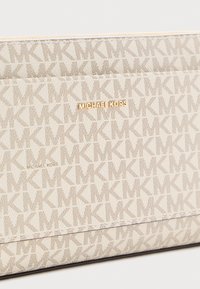 Šviesiai kreminė Michael Kors piniginė su pasikartojančiu MK logotipo raštu ir auksine metaline Michael Kors vardo plokštele.
