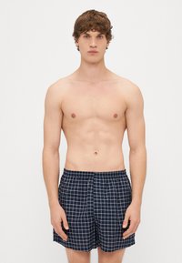 Ναυτικά μαγιό με λευκό σχέδιο πλέγματος, ελαφρύ ύφασμα, ελαστική μέση και πλαϊνές τσέπες. Λείο υφή, χαλαρός σχεδιασμός.