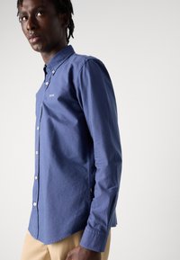 Navyblauw langemouwen shirt met button-down kraag, knopen aan de voorkant en een subtiel logo. Gladde katoenstof met een gelijkmatige textuur.