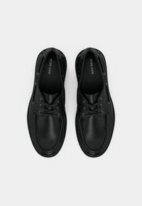 Μαύρα δερμάτινα παπούτσια με στρογγυλή μύτη, αντιθετική ραφή και μεταλλικά περφορέ για τα κορδόνια. Ομαλή υφή και μινιμαλιστικός σχεδιασμός.