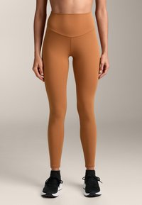 Rjave legice visoke pasu, narejene iz raztegljivega blaga, brez šivov, v kombinaciji s črnimi športnimi čevlji z belimi poudarki.