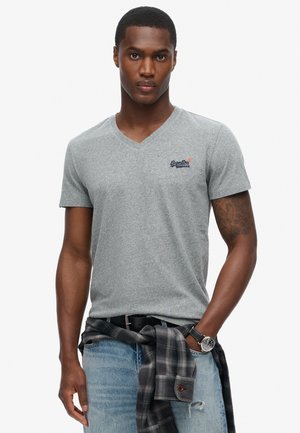 Gray v-neck t-shirt made of soft fabric with short sleeves. Features embroidered logo on left chest, paired with blue jeans and a flannel shirt tied at waist.