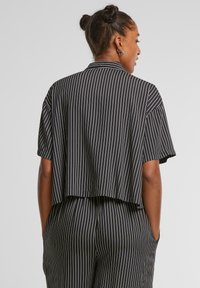 Cropped shirt a righe bianche e nere con maniche corte e colletto. Realizzato in tessuto leggero, presenta un orlo dritto e una vestibilità ampia.