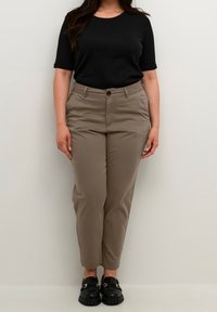 Sort kortærmet t-shirt, beige skræddersyede bukser med en knap og sorte loafers med guld accenter. Glat stof, tætsiddende pasform.