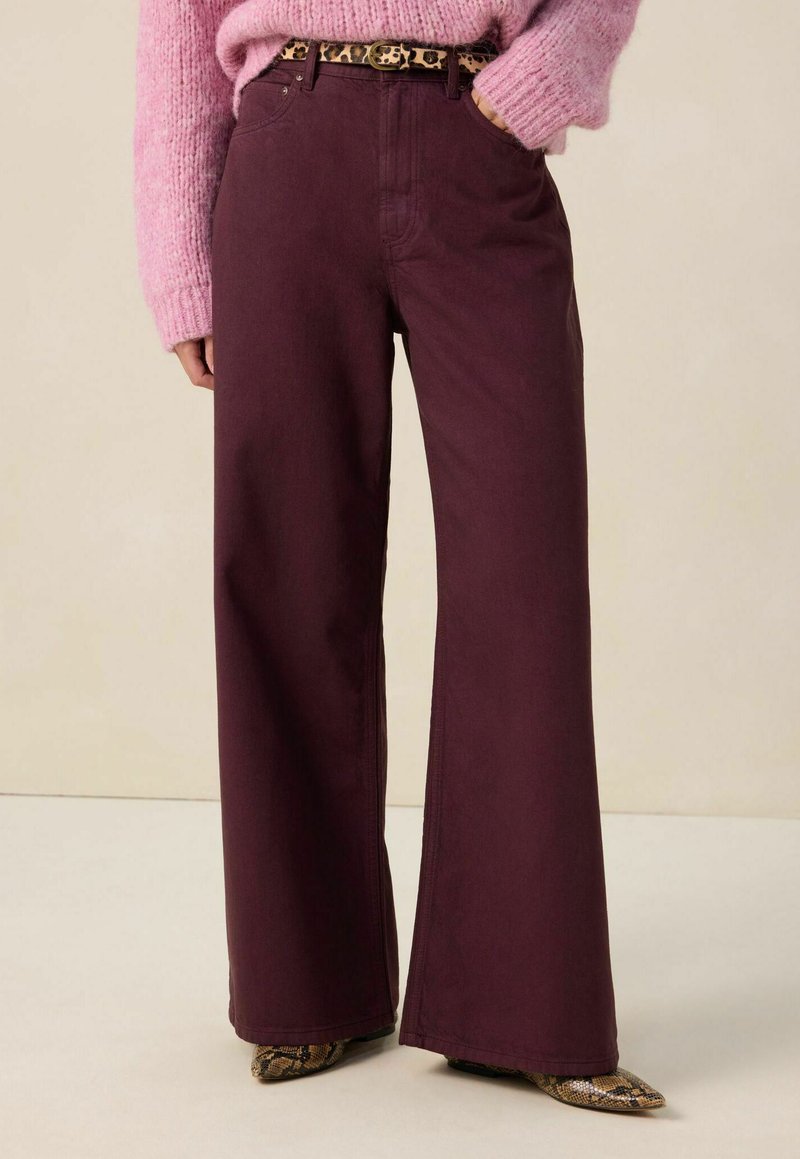 Jean large bordeaux avec une finition texturée, doté de cinq poches et d'une ceinture à motif léopard. Associé à des chaussures en cuir de serpent à bout pointu.