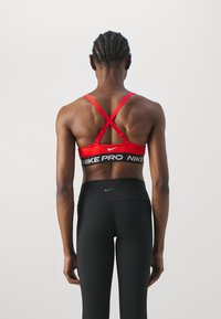 Sujetador deportivo rojo con tirantes cruzados en la espalda, cinturilla negra con el texto "NIKE PRO", combinado con leggings negros de cintura alta, de textura suave.