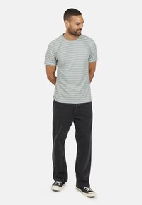 T-shirt rayé gris en coton, avec des manches courtes et un col rond. Associé à un jean noir et des baskets en toile.