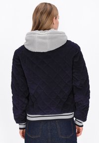 Granatowa pikowana kurtka ze sztruksu z szarą polarkową kapturem, ściągaczami na mankietach i u dołu. Charakteryzuje się wzorami w romby i miękką fakturą.