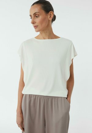 White loose-fit top with short flutter sleeves, rounded neckline, soft texture. Paired with light brown, elastic-waist pants.