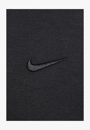 Must musträtikaga kangas, millel on sooneline tekstuur, sisaldab väikest, tikkitud Nike'i swooshi logo tumedamas mustas varjus.