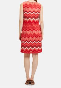 Czerwona sukienka bez rękawów w wzór chevron w odcieniach czerwieni, różu i bieli. Gładka tekstura, do kolan, dopasowany fason.