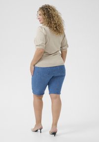 Beige top met korte mouwen en pofschouders, gecombineerd met blauw gestreepte denim shorts met een middelhoge taille en achterzakken.