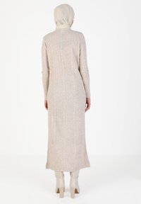 Robe longue à côtes beige avec un col haut et des manches longues. Présente un détail de boutons dans le dos. Associée à des bottines couleur crème.