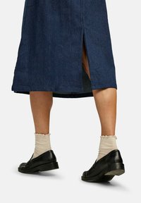 Fustă din denim albastru închis cu o fenda în spate, asortată cu pantofi negri și șosete crem cu model rip.