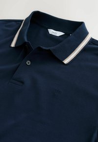 Dunkelblaues Poloshirt aus strukturiertem Stoff, mit einem zweifarbigen Kragen in Weiß und Beige gestreift, einer Knopfleiste mit einem einzigen Knopf und einem gestickten Logo.