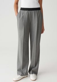 Persona che indossa dei pantaloni grigi larghi con una vita elastica nera, scarpe da ginnastica bianche e una maglietta bianca senza maniche, in piedi con le mani nelle tasche.