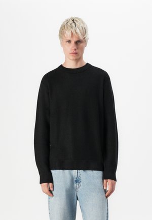 Zwarte trui met een gestructureerd gebreid patroon, geribbelde halslijn en mouwen, gecombineerd met lichtblauwe jeans. Eenvoudig, klassiek ontwerp.