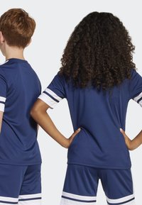 Maillots de sport navy avec des accents rayés blancs, tissu lisse, design à col rond, portés par deux enfants vus de dos.