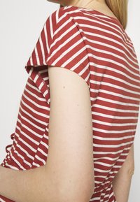 Rot-weiße gestreifte Kurzarmbluse mit rundem Halsausschnitt und seitlichem Raffungselement, aus weichem Baumwollstoff gefertigt.
