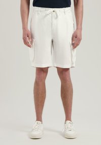 Weiße Cargo-Shorts aus strukturiertem Stoff, mit Kordelzugbund, Seitentaschen und lockerer Passform. Getragen mit weißen Turnschuhen.