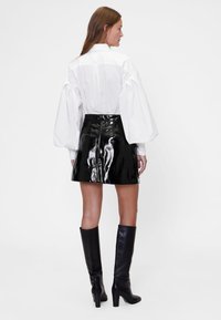 Bela prevelika srajca z napihnjenimi rokavi, kombinirana s sijočo črno vinil mini krilom in črnimi škornji s peto do kolen.