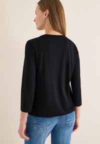 Top noir à manches longues avec une coupe décontractée et un col rond, associé à un jean bleu. Tissu texturé aux manches et à l'ourlet.