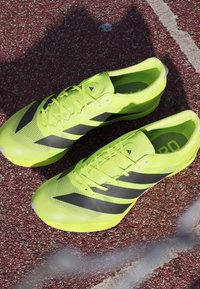 Lime green athletic shoes with black diagonal stripes, lightweight mesh fabric, flat soles, and lace-up design. Suitable for track use.