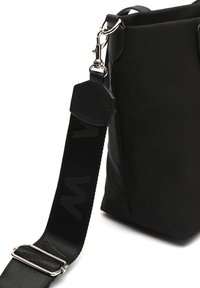 Crna najlonska torba s teksturiranim kožnim detaljima i odvojivim, podesivim remenom s suptilnim uzorkom loga.