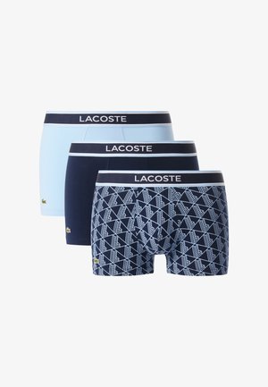 Tres pares de bóxer Lacoste: uno azul claro, uno azul marino oscuro y uno azul marino con un patrón geométrico blanco; todos cuentan con cinturillas elásticas.