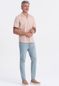 Korte mouwen, lichtroze shirt met een geknipt kraagje, gecombineerd met lichtblauwe jeans en bruine instapschoenen. Gladde stof, casual pasvorm.
