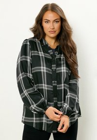 Camicia a quadri nera e grigia con maniche lunghe e gonfie e davanti con bottoni. Presenta polsini arricciati e una texture del tessuto liscia.