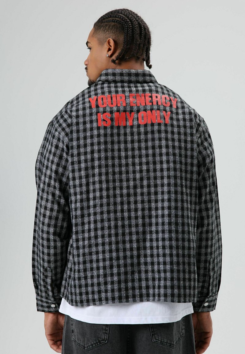 Zwart-grijs geruit flanellen jack met een rode tekstprint op de bovenrug. Zachte stof, lange mouwen en manchetten met knopen.