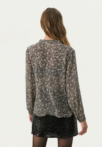Bluza dugih rukava od prozirnog crnog materijala sa cvjetnim i paisley uzorcima, s okruglim izrezom i lagano širokim krojem.