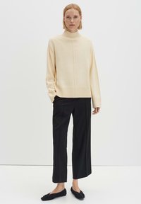 Beiger Rollkragenpullover mit geripptem Saum und Bündchen, kombiniert mit schwarzen weiten Hosen und schwarzen flachen Schuhen. Einfaches, klares Design.