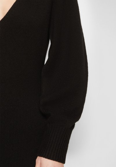 Suéter de malha preto com um decote em V profundo e mangas volumosas. Tecido texturizado com punhos canelados. Enfoque no detalhe das mangas.