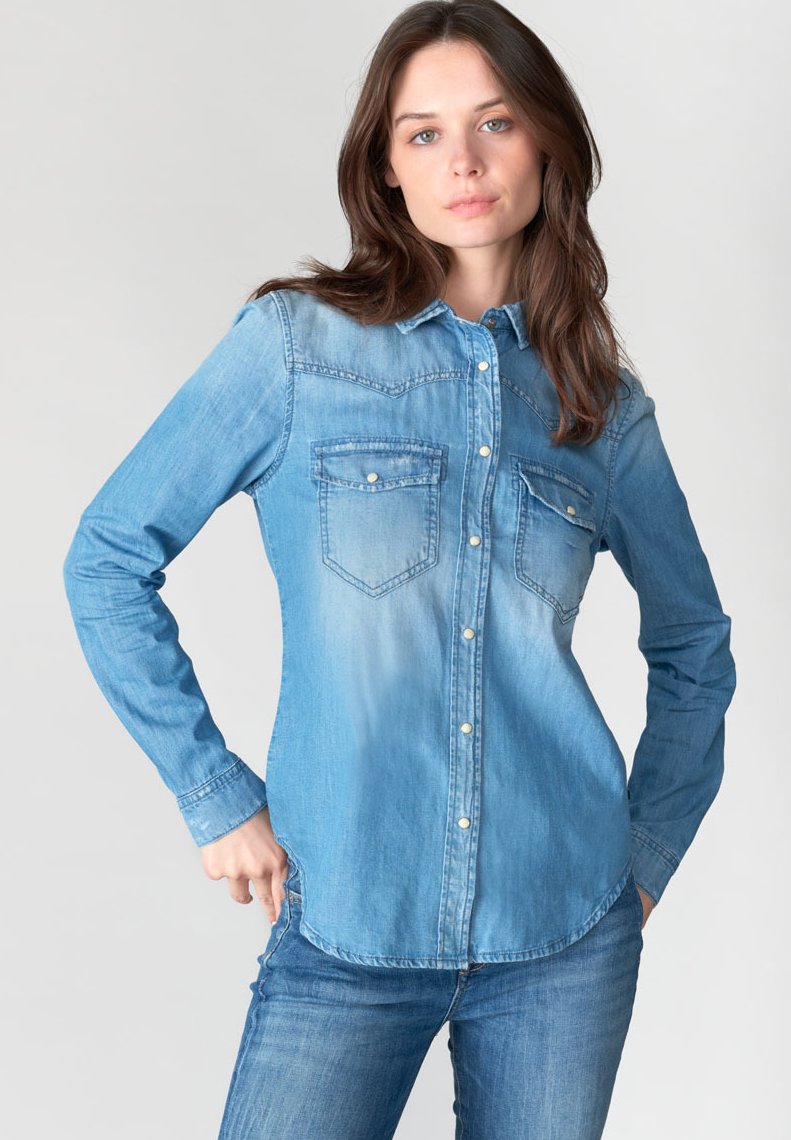 Chemise en denim bleu clair à manches longues, fermeture à boutons sur le devant, deux poches poitrine, ourlet arrondi et décoloration vers le centre.