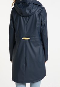Manteau imperméable marine avec capuche, manches longues et ceinture à la taille ornée d'un accent décoratif doré. Surface lisse et design minimaliste.