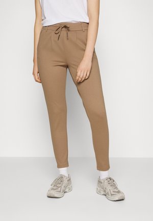 Pantalons jogger beige avec une ceinture à cordon, coupe slim et tissu doux. Portés avec un t-shirt blanc et des baskets claires.
