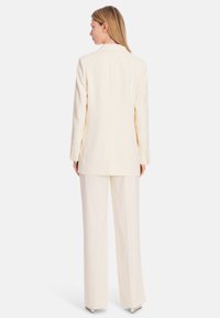 Light beige tailored suit featuring a long blazer with a notched collar and wide-leg trousers; smooth texture with subtle stitching details.