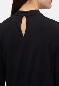 Svart blus med hög krage, detalj med nyckelhål baktill och två svarta knappstängningar vid halsen. Slätt, lätt tyg.