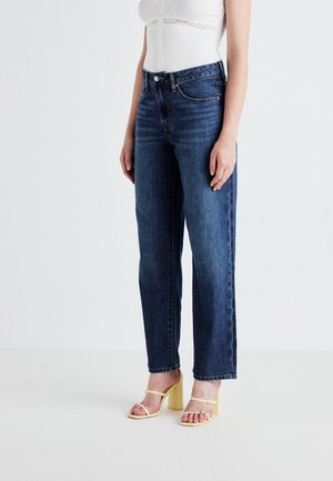 Høyt liv, rett ben blå jeans med en liten falming. Kombinert med en tettsittende hvit topp og gule høyhælte sandaler.