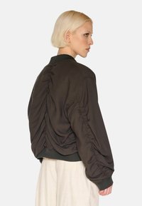 Braune Bomberjacke mit einem gerafften Rückendesign, geripptem Kragen und Bündchen sowie strukturiertem Stoff. Verfügt über eine lockere Passform und übergroße Ärmel.