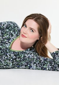 Blusa floreale con sfondo scuro e motivi floreali verdi e bianchi, scollatura rotonda con bordino verde e maniche lunghe.