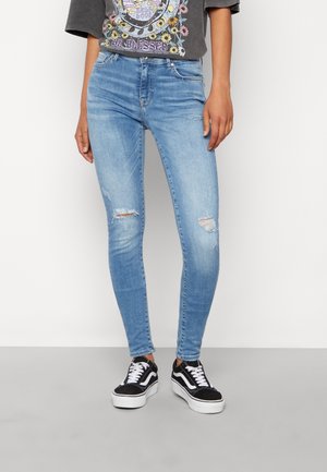 Person wearing light blue ripped skinny jeans, black and white sneakers, and a dark grey graphic t-shirt with floral and text design.