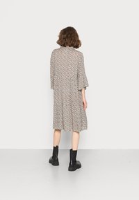 Robe à imprimé floral beige avec manches courtes évasées et jupe évasée ; associée à des bottines noires. Tissu lisse, coupe décontractée.