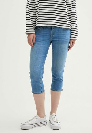 Ljusblå denim capribyxor med slim fit och fransad fåll, kombinerat med vita kanvas sneakers och en långärmad topp med svart-vita ränder.